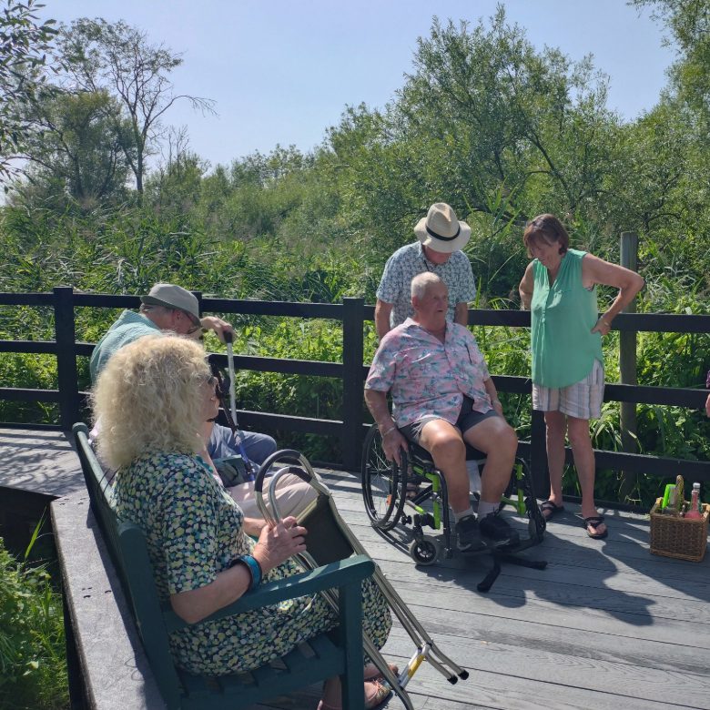Members of MIGGs enjoying the area by the kingfisher hide, seated on the bench. In the centre, a MIGGS member is in his wheelchair. Previously, this area inaccessible to people who use wheelchairs.